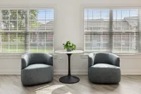 Elegant and bright seating area featuring two modern gray chairs, a sleek round table, and large windows with scenic outdoor views.