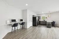 Bright, contemporary shared workspace with sleek kitchen setup, featuring elegant bar stools and state-of-the-art computers.