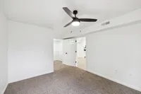 Bright and airy bedroom featuring a modern ceiling fan, plush carpeting, and a walk-in closet with white shelving.