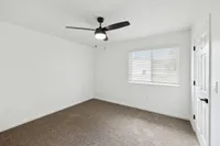 Bright and inviting room with modern ceiling fan, large window with blinds, and plush carpet flooring.