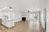 Bright and airy open-concept living space featuring elegant hardwood floors, a modern kitchen with sleek white cabinetry, and a cozy fireplace.