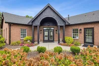 Charming brick building entrance with elegant black accents, surrounded by vibrant landscaping and colorful flowers, under a clear blue sky.