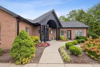 Charming brick apartment building with elegant entrance, surrounded by lush greenery and vibrant flowers in a serene setting.