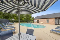 Inviting outdoor pool area with sleek loungers and striped umbrellas, nestled beside a charming brick building.