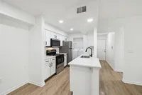 Modern kitchen boasting sleek white cabinetry, stainless steel appliances, and elegant wood flooring, leading to a convenient laundry area.