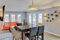 Elegant dining area with modern decor, featuring a sleek wooden table, stylish chairs, and a vibrant orange sofa by large windows with serene outdoor views.