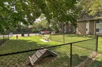 Charming apartment complex featuring a lush, fenced dog park with seating area and vibrant greenery.