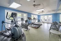 Bright fitness center featuring modern gym equipment, treadmills, and an elliptical, with a refreshing blue accent wall and natural light streaming in.