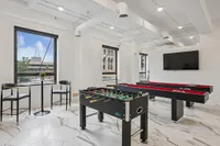 Contemporary recreation room with a foosball table, pool table, and flat-screen TV, featuring large windows and sleek marble floors.