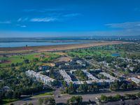 Aerial view of a vibrant apartment community surrounded by lush greenery, lake, and cityscape, offering an idyllic blend of nature and urban living.