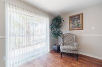 Bright and inviting corner with a stylish armchair, decorative plant, and large window featuring vertical blinds, overlooking a lush outdoor view.