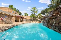 Inviting apartment complex pool area with a stunning waterfall feature and comfortable lounging chairs, surrounded by lush greenery and classic brick architecture.