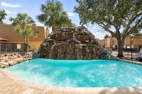 Inviting outdoor pool with cascading waterfall feature and lush palm trees, offering a tropical oasis ambiance at the apartment complex.