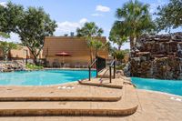 Inviting outdoor pool area with scenic waterfall feature, surrounded by lush palm trees and comfortable lounge seating, perfect for relaxation.