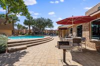 Inviting outdoor area featuring a sparkling pool, shaded patio with red umbrellas, and lush palm trees, perfect for relaxation and entertainment.