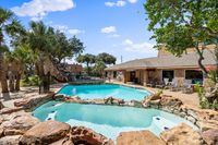 Inviting apartment complex pool area with cascading waterfall, surrounded by lush greenery and modern lounge chairs.