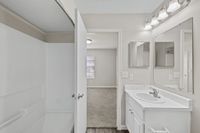 Bright and modern bathroom with elegant fixtures, white marble countertop, and a spacious shower area next to a cozy carpeted bedroom.