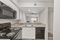 Modern kitchen with sleek granite countertops, black appliances, and open-plan design leading to a bright living area.