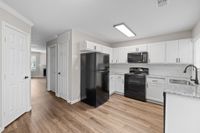 Bright and modern kitchen with sleek black appliances, white cabinetry, and hardwood floors opening into a cozy living area.