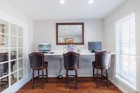 Bright and welcoming home office space with elegant wooden chairs, modern computer setups, and large window bringing in natural light.