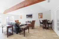 Elegant living room with vaulted ceiling and wooden beam, featuring plush seating, sleek leather sofas, and sophisticated dark wood furniture, bathed in natural light from large windows.