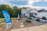 Charming two-story home with a beautifully landscaped front yard, open house signs, and a sunlit driveway, perfect for modern living.