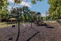 Inviting outdoor playground surrounded by lush greenery, featuring swings, slides, and a charming wooden gazebo.