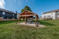 Charming outdoor pavilion with wooden structure set in a spacious grassy backyard, perfect for relaxing and entertaining.