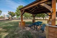Charming outdoor space showcasing a wooden pavilion with picnic tables, perfect for family gatherings, next to a fenced playground surrounded by lush greenery.