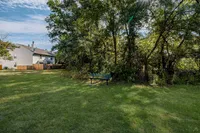 Charming backyard view featuring lush greenery, a cozy bench, and ample open space for relaxation.