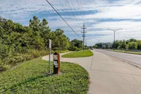 Scenic sidewalk view with lush greenery and clear skies, showcasing a peaceful suburban pathway ideal for walking and biking.