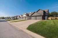 Charming suburban street lined with modern townhouses, each featuring double garages and neatly manicured lawns under a clear blue sky.