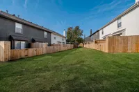 Charming townhouse backyard with lush green grass and private wooden fences under a clear blue sky.