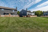 Spacious backyard view of modern townhomes featuring fenced patios, lush green lawn, and a clear blue sky.