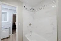 Elegant bathroom showcasing modern white marble tile, a chic bathtub, and a sleek vanity with illuminated mirror, enhancing the sophisticated ambiance.