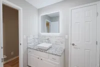 Modern bathroom featuring an illuminated mirror, elegant gray granite countertop, and stylish white cabinetry.