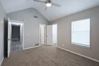 Bright and spacious bedroom with vaulted ceiling, modern fan, and plush carpet, featuring ample natural light through a large window.