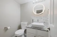 Modern bathroom featuring a circular backlit mirror, sleek vessel sink, and elegant marble countertop.