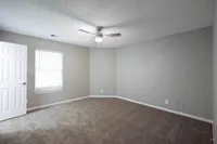 Bright and spacious empty bedroom featuring plush carpeting, a modern ceiling fan, and elegant neutral walls, perfect for personalization.