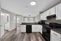 Sleek modern kitchen with stylish white cabinets, black appliances, and spacious open layout seamlessly connecting to the well-lit living area.