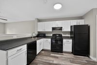 Modern kitchen with sleek black appliances, white cabinetry, and elegant laminate flooring.