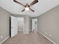 Inviting bedroom with cozy carpet, neutral walls, and a modern ceiling fan, leading to a spacious walk-in closet.