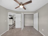 Inviting bedroom featuring a modern ceiling fan, plush carpeting, and access to a bright hallway leading to the kitchen with stylish flooring.