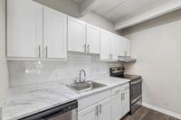 Modern kitchen with sleek white cabinetry, marble countertops, and stainless steel appliances in a stylish apartment.