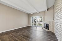 Inviting living room with sleek hardwood floors, stylish white brick fireplace, and expansive sliding glass doors leading to a beautiful garden view.