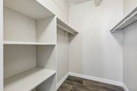 Spacious walk-in closet with sleek white shelving and modern wooden flooring, offering ample storage space.