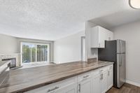 Bright living area with modern kitchen, featuring sleek countertops, stainless steel fridge, and large sliding glass doors opening to balcony with lush green views.