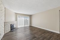 Spacious living room featuring elegant wood flooring, a cozy fireplace, and large sliding glass doors with vertical blinds.