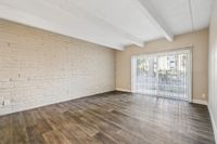 Bright and airy living room with wood-style flooring, exposed brick accent wall, and floor-to-ceiling sliding glass doors leading to a scenic outdoor view.