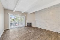 Bright living room with large windows, wooden floors, and a cozy brick fireplace, perfect for relaxation.